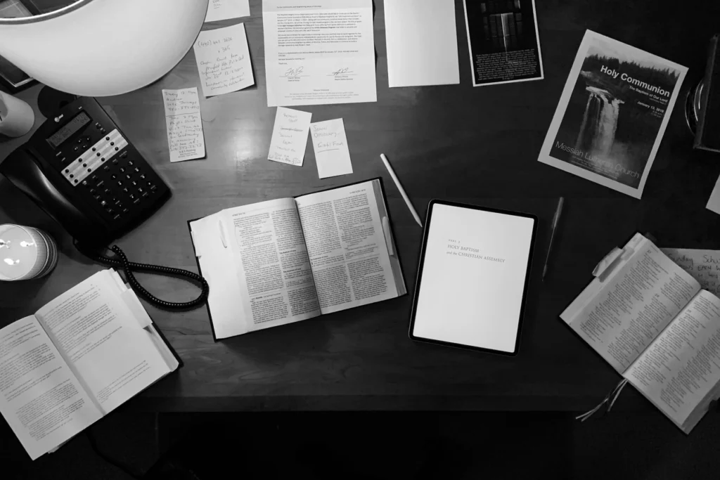 A black-and-white research desk with books, notes, a tablet, and a telephone